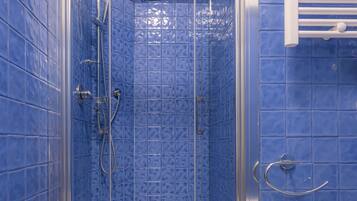 Une douche fermée par des parois de verre, avec des murs recouverts de carreaux bleus et un lavabo blanc.