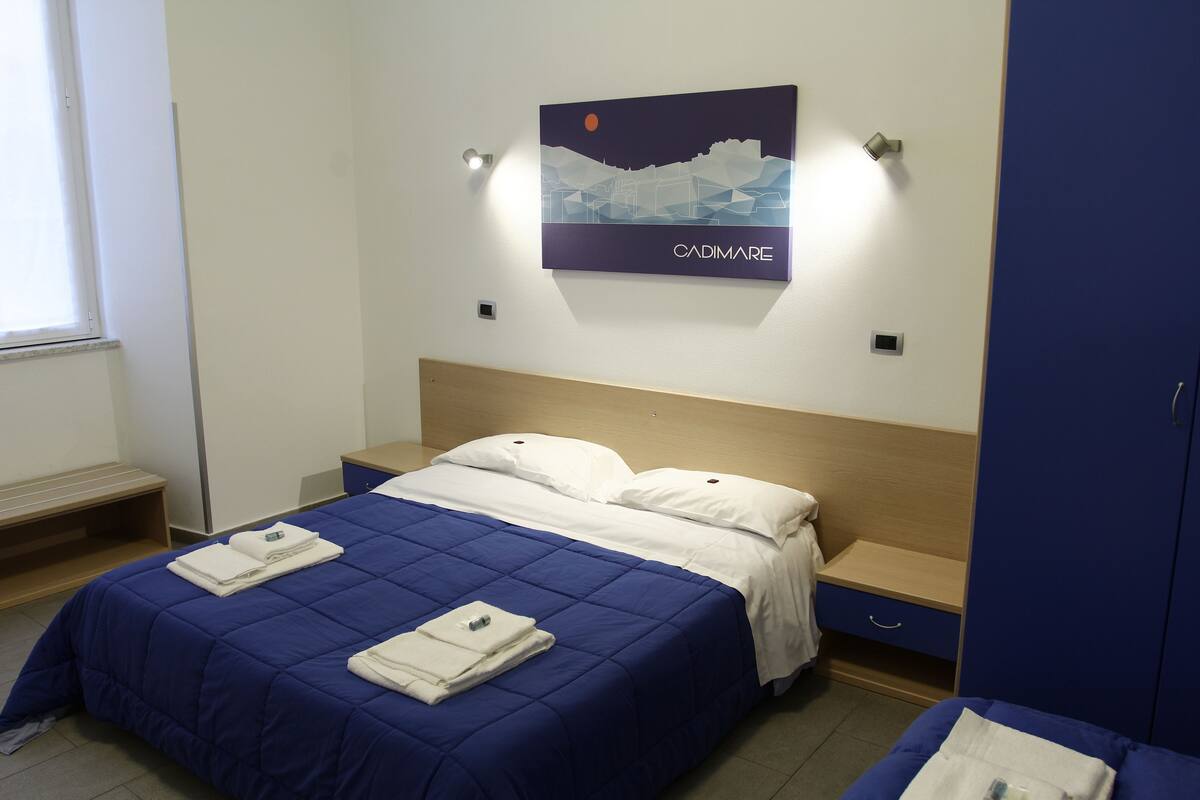 A hotel room with a bed, a nightstand, a wardrobe, and a wall-mounted artwork.