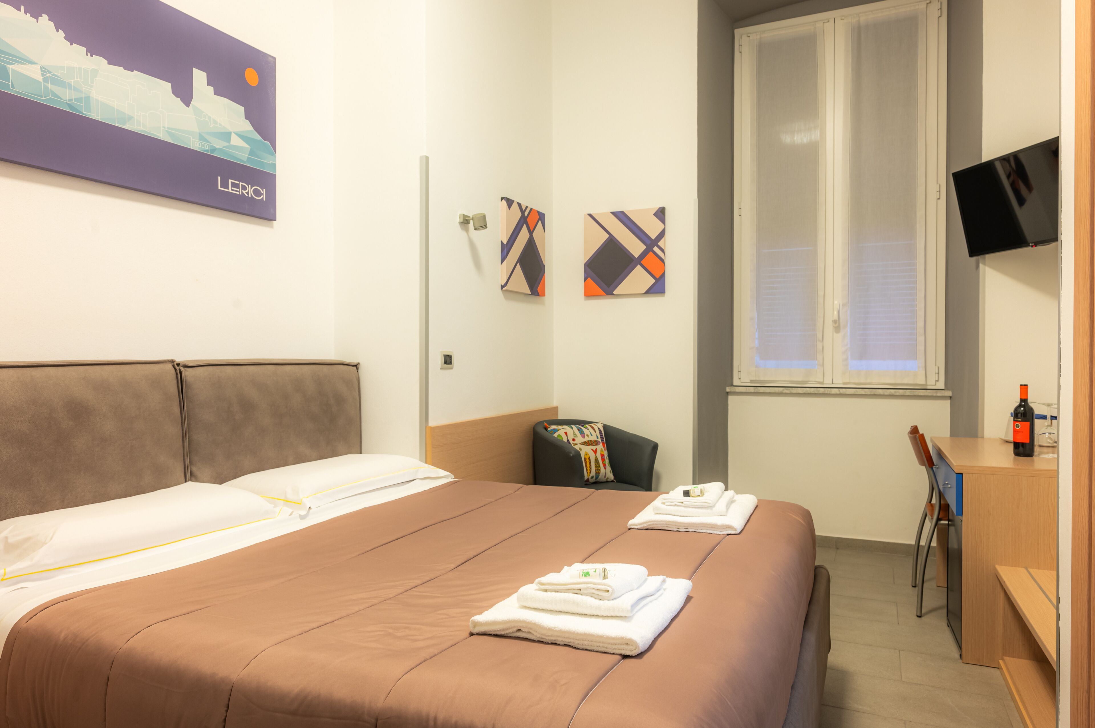 Een hotelkamer met een groot bed, een bureau, een stoel, een televisie en kunstwerken aan de muur.