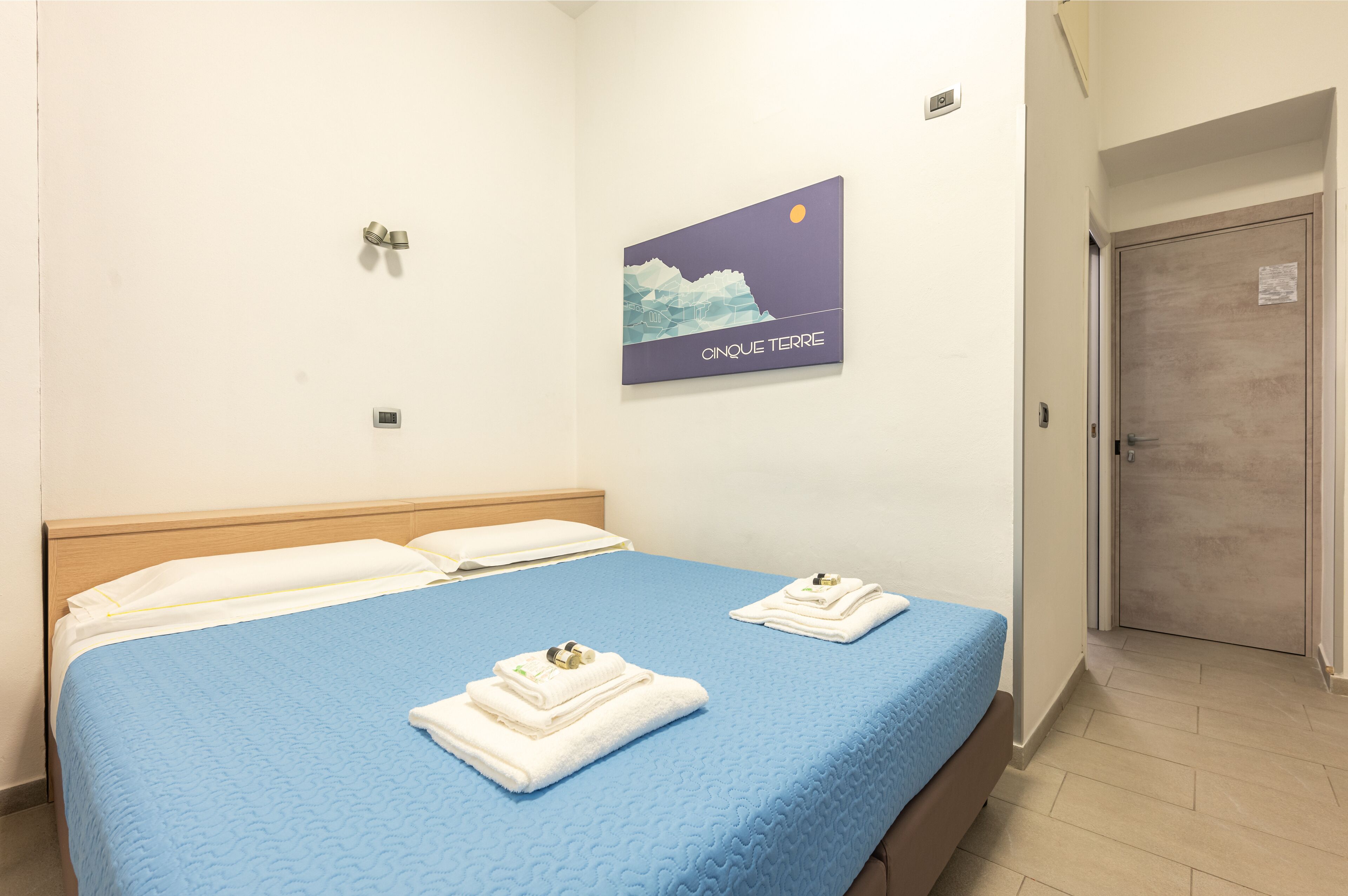 Une chambre d’hôtel avec un lit, deux serviettes, un interrupteur fixé au mur et une porte.