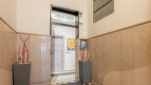 A hallway with a tiled floor, a door leading to a room, and two planters with red and white sticks. - Affittacamere del Golfo e delle Cinque Terre (La Spezia)