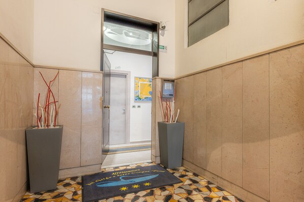 A hallway with a tiled floor, a door leading to a room, and two planters with red and white sticks. - Affittacamere del Golfo e delle Cinque Terre (La Spezia)