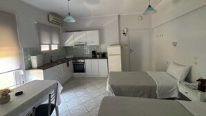 A compact kitchen with white cabinets, a dining table, and two beds. - Eliza Apartments (Rethymno)