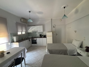 A compact kitchen with white cabinets, a dining table, and two beds.