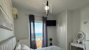 Un dormitorio con cama, cómoda, espejo, televisor y vista al mar.