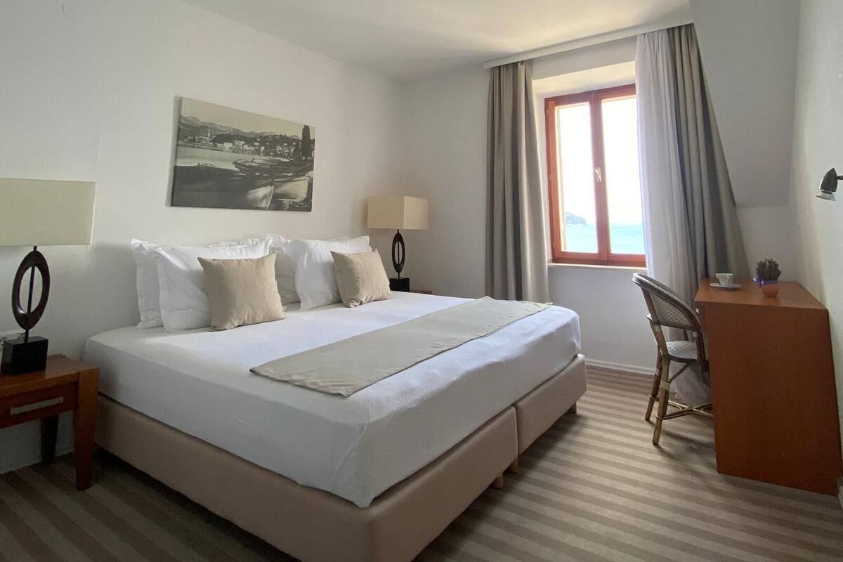 A hotel room with a large bed, a desk, a chair, a lamp, and a window with curtains.