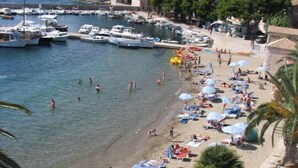 Una spiaggia con barche ormeggiate, persone che nuotano e bagnanti sulla sabbia.