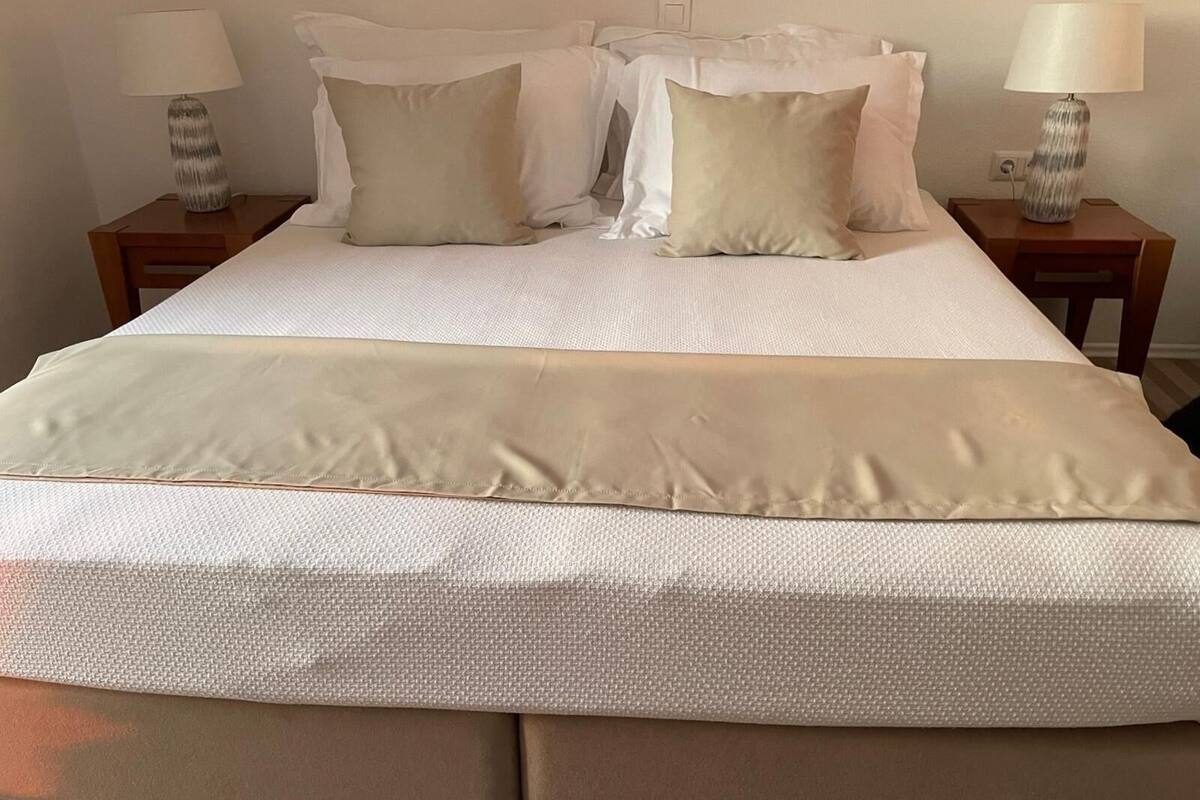 A neatly made bed with a white textured bedspread and two pillows. There are two bedside tables with lamps on either side of the bed.