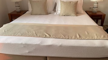 Un lit bien fait, recouvert d’une courtepointe blanche à texture intéressante, et agrémenté de deux oreillers. De part et d’autre du lit, on trouve deux tables de chevet sur lesquelles sont posées des lampes.
