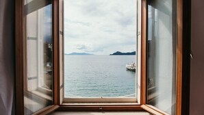 Vista attraverso una finestra con cornice in legno, su un mare calmo con una barca e terra in lontananza.