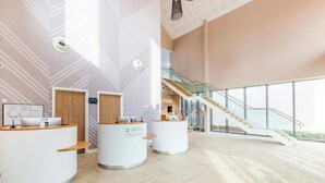 A spacious lobby with a high ceiling, a staircase, and reception desks. - Peter Scott House, Birmingham (Birmingham)