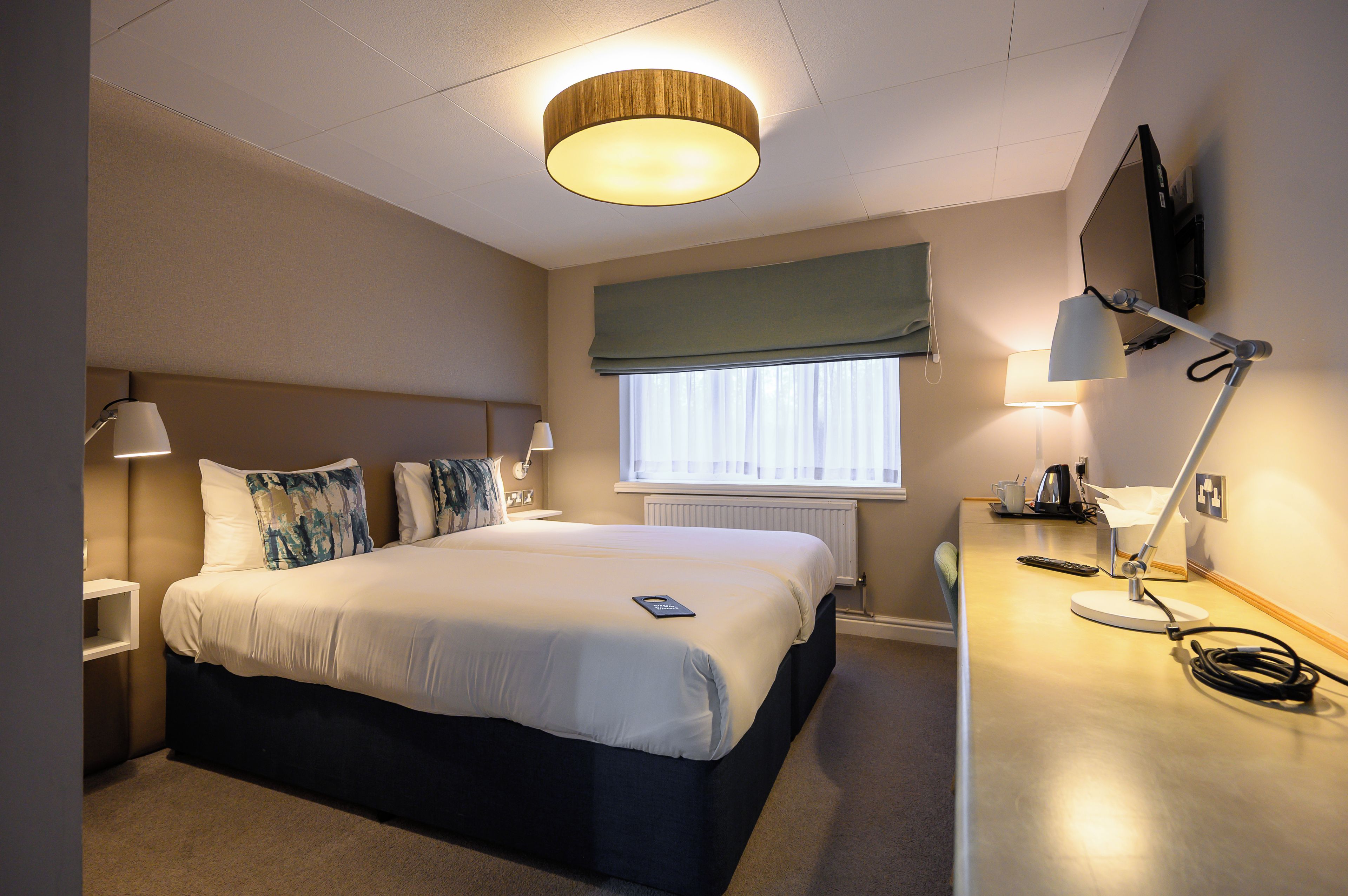 A hotel room with a bed, bedside lamps, a desk with a lamp, a television, and a window with curtains.