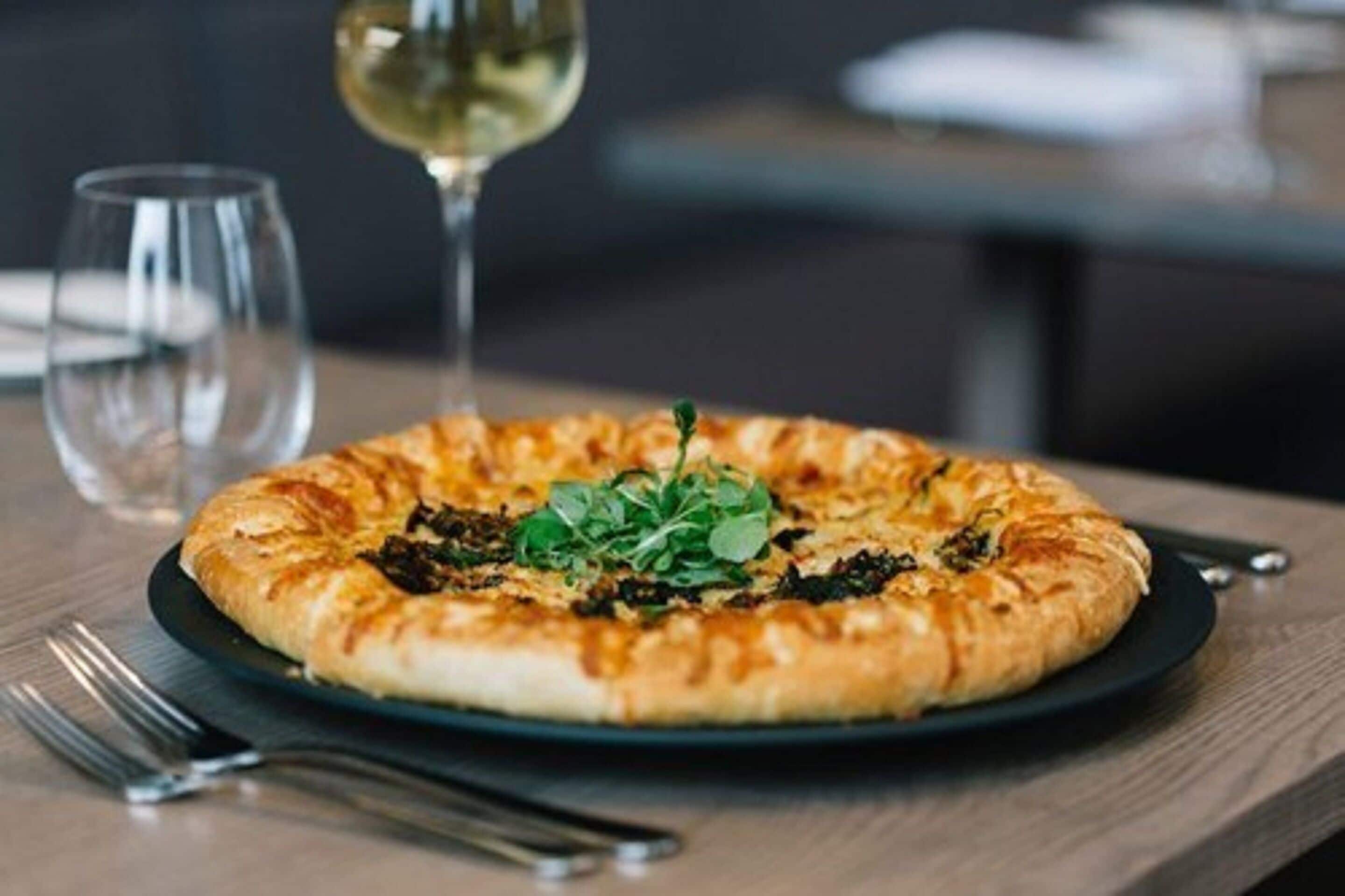 Una pizza sobre un plato negro, con un tenedor y un cuchillo a un lado.