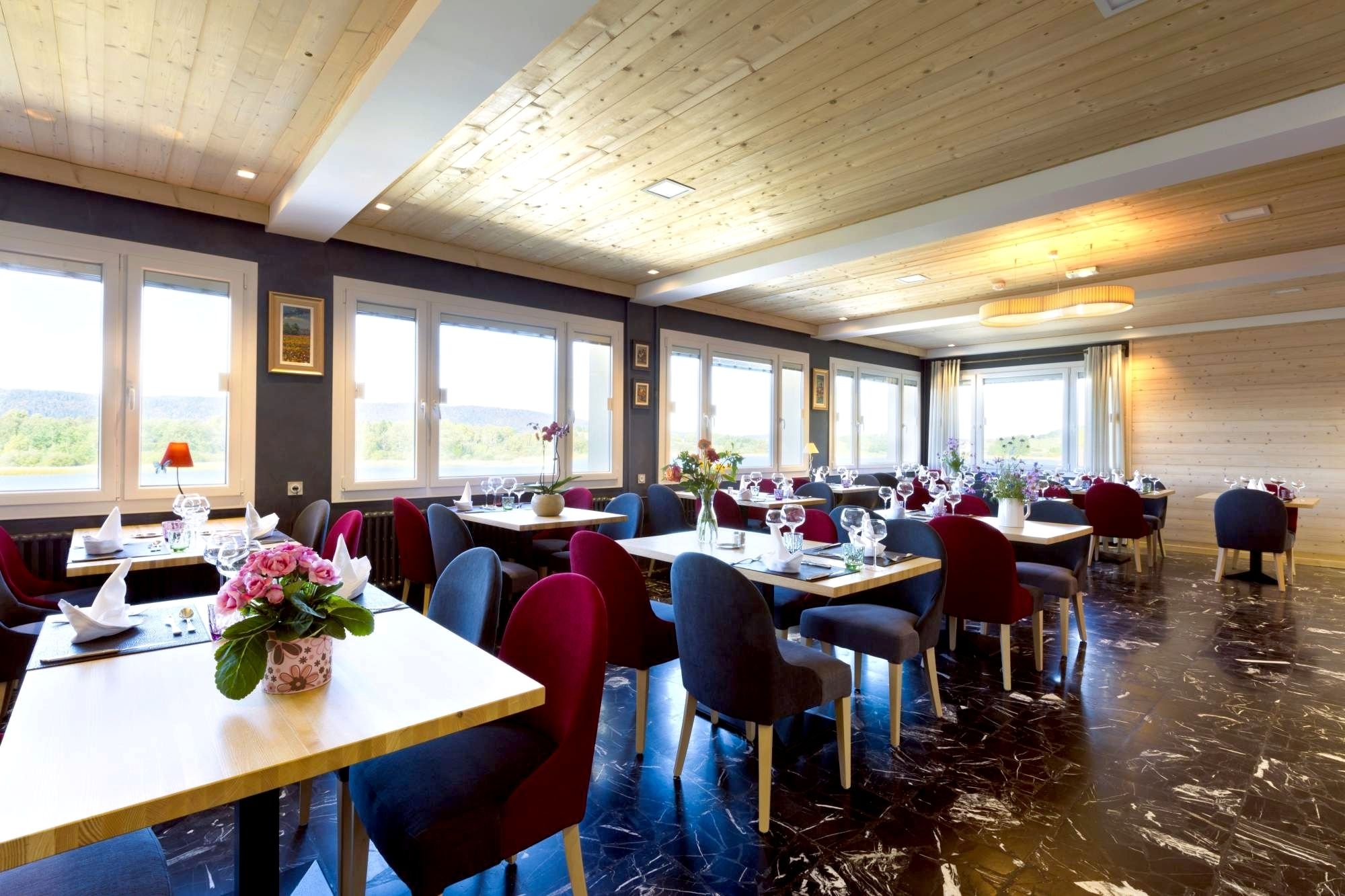 Un restaurant doté de nombreuses tables et chaises, de grandes fenêtres offrant une vue dégagée et d’un plafond en bois.