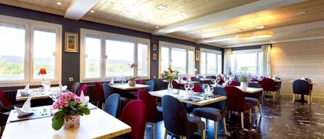 Un restaurant doté de nombreuses tables et chaises, de grandes fenêtres offrant une vue dégagée et d’un plafond en bois.