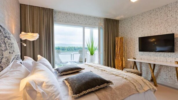 A modern bedroom with a large bed, a TV, and a balcony view. - Hotel de l'Abbaye (Grande-Rivière-Château)