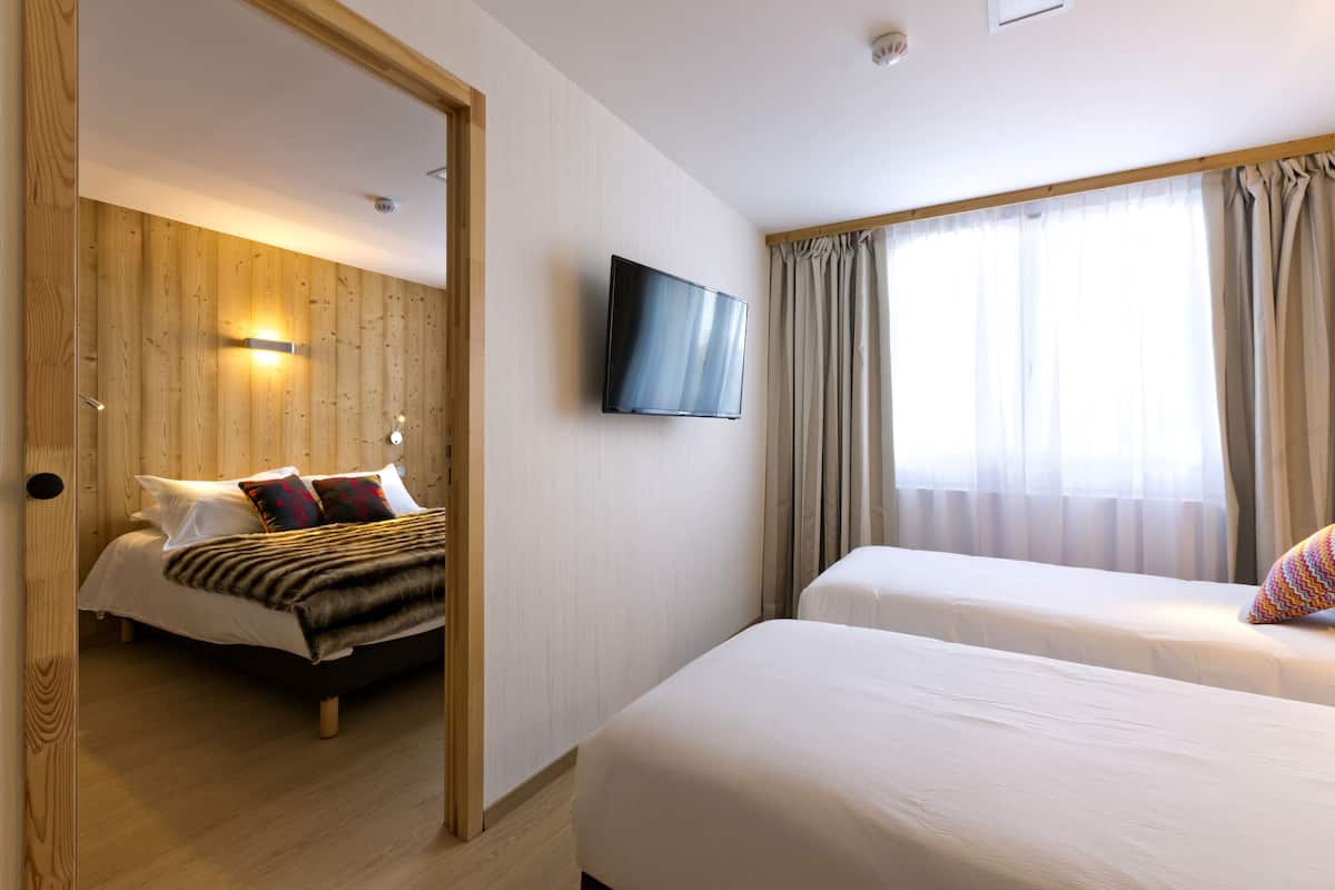 A hotel room with a wooden wall, a flat-screen TV mounted above a bed, and a window with curtains.