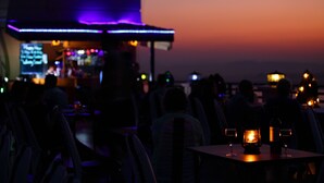 A dimly lit outdoor seating area with tables and chairs, a bar in the background, and a sunset in the distance. - Ayarwaddy River View Hotel (Mandalay)