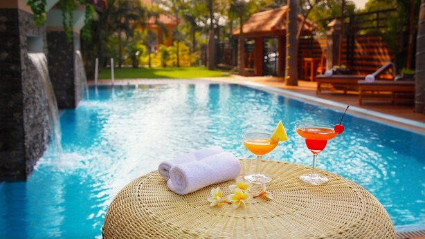 A poolside setting with a wicker table, a towel, and two drinks. - Ayarwaddy River View Hotel (Mandalay)