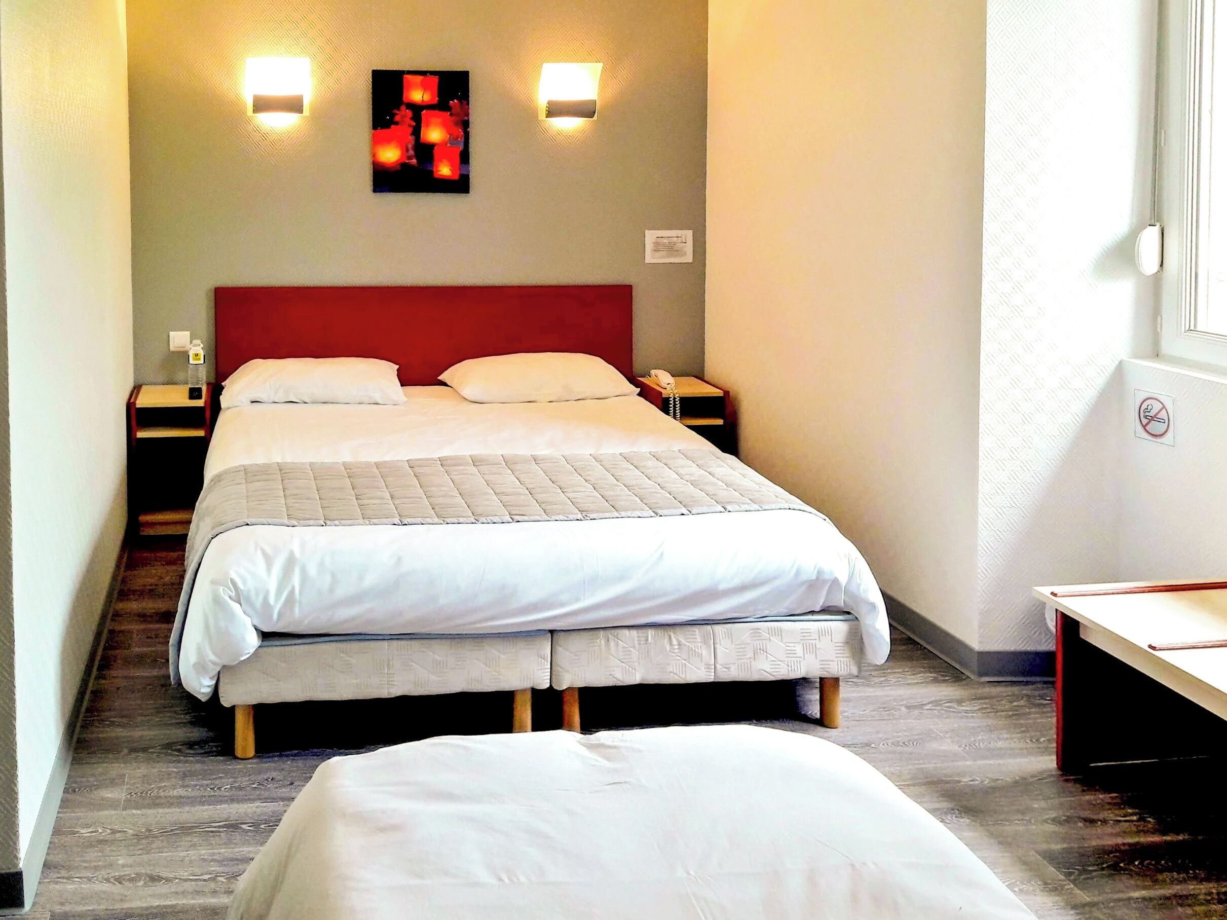 Quarto de hotel com cama, duas mesas de cabeceira, luminária na parede e janela com vista.