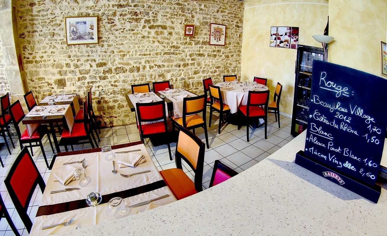 A restaurant with stone walls, red and black chairs, and tables set for dining. A chalkboard menu is visible on the right.