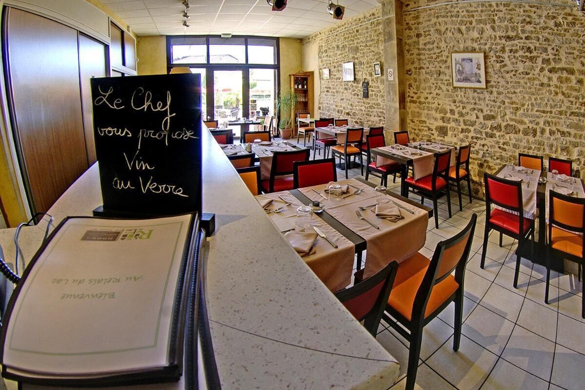 A restaurant with stone walls, tables set with red chairs, and a chalkboard menu.