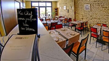 Un restaurant aux murs de pierre, avec des tables ornées de chaises rouges et un menu écrit à la craie sur un tableau noir.