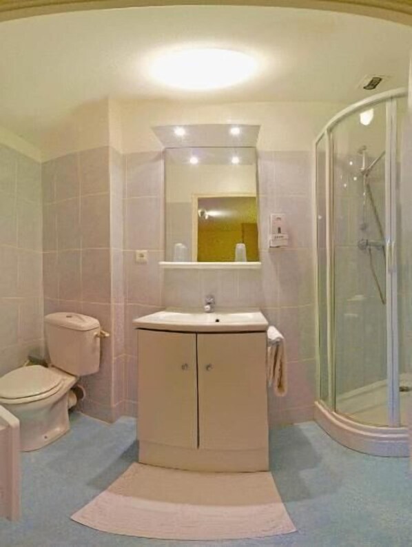A bathroom with a toilet, sink, mirror, and glass shower enclosure.