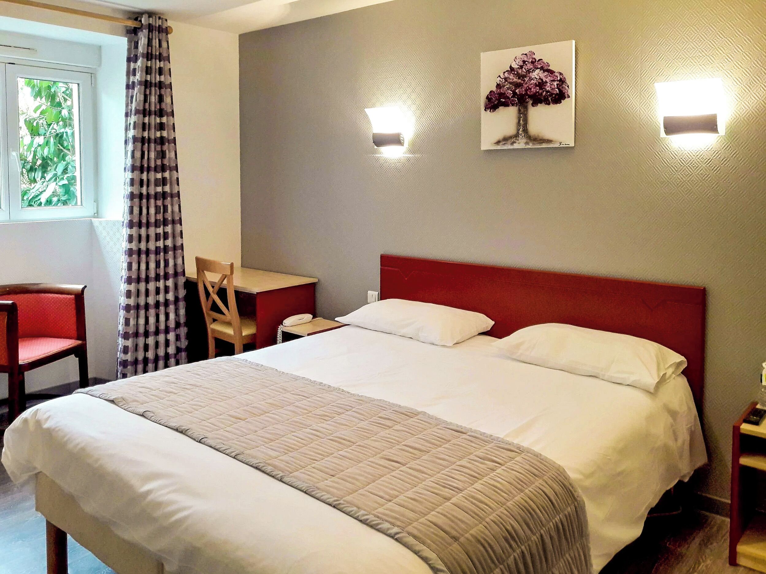 Quarto de hotel com uma cama grande, uma escrivaninha, uma cadeira e uma janela com cortinas.