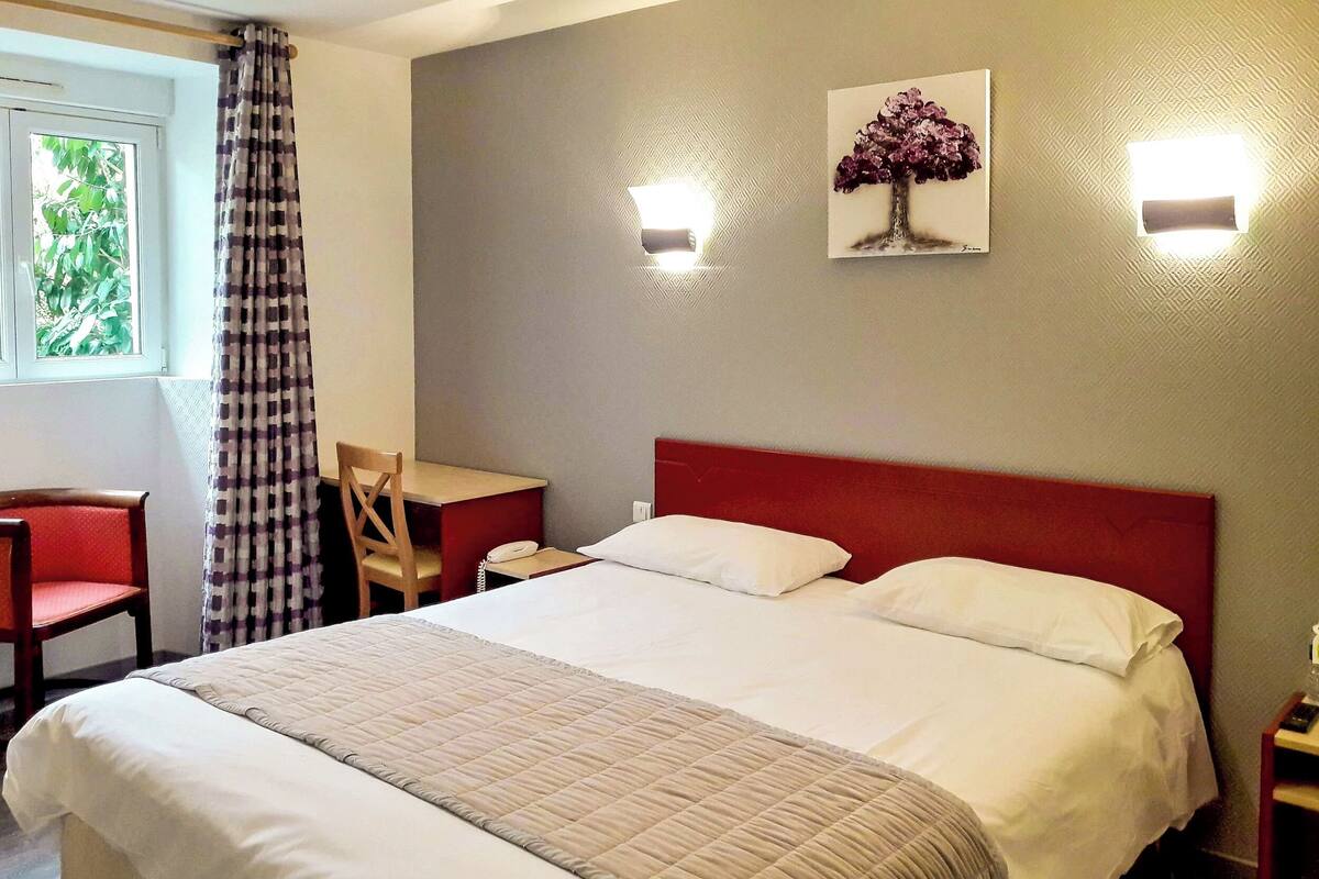 Habitación de hotel con una cama grande, un escritorio, una silla y una ventana con cortinas.