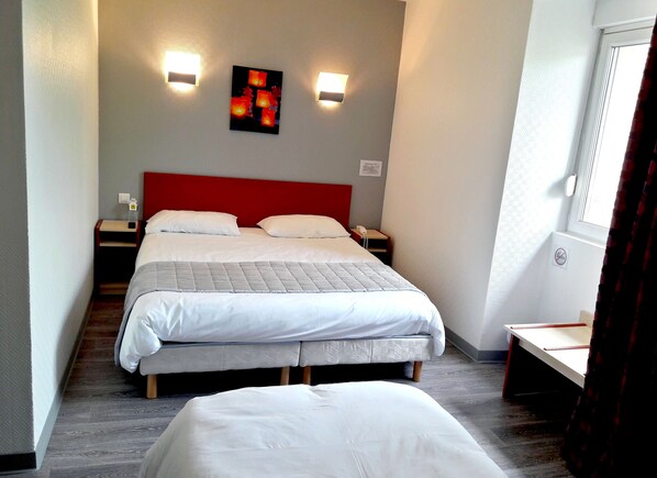 Una habitación de hotel con una cama grande, dos mesitas de noche, un cabecero rojo y dos luces fijadas a la pared.