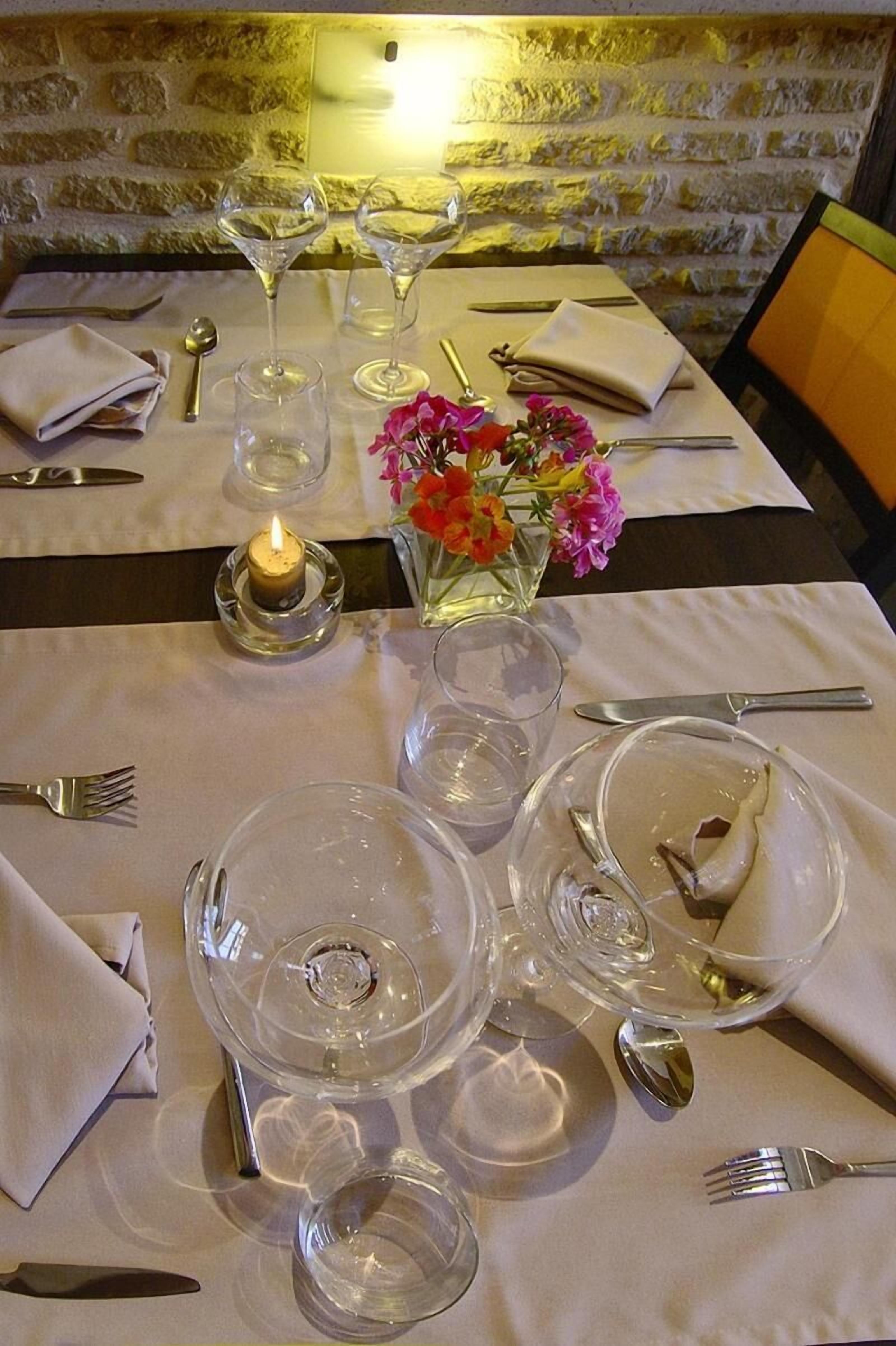 A dining table set with wine glasses, plates, and cutlery, a candle, and a vase with flowers.