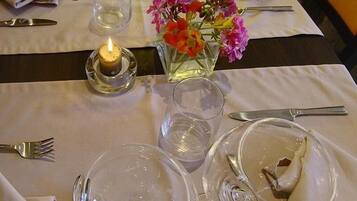 A dining table set with wine glasses, plates, and cutlery, a candle, and a vase with flowers.