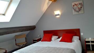 A bedroom with a sloped ceiling, a bed with white and red bedding, a wooden headboard, a nightstand with a lamp, and a wall-mounted light.