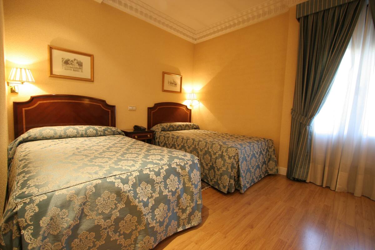 Camera d'albergo con due letti, testiere in legno e lampade a parete.