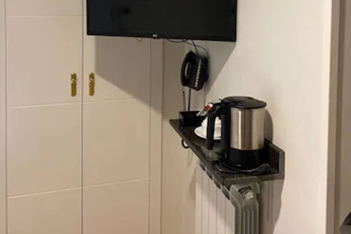 Una stanza con una porta bianca, una televisione a muro e una macchina del caffè su uno scaffale.