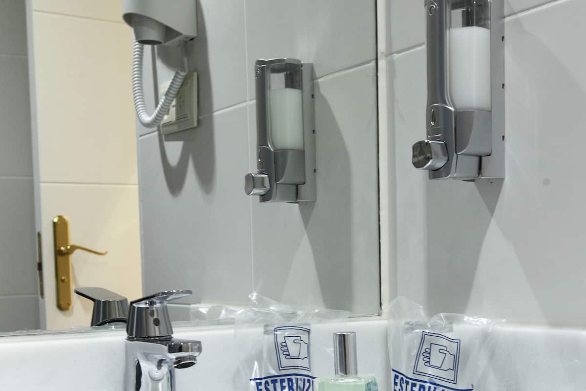 Un lavabo con uno specchio, un rubinetto e due erogatori di gel disinfettante con l'etichetta 'ESTERILIZAD'.