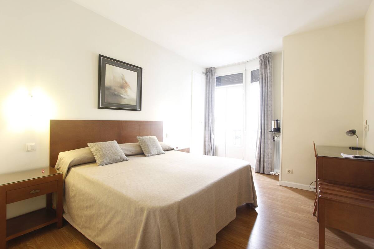 Una camera d'hotel con un letto grande, un comodino, una scrivania e una finestra con tende.
