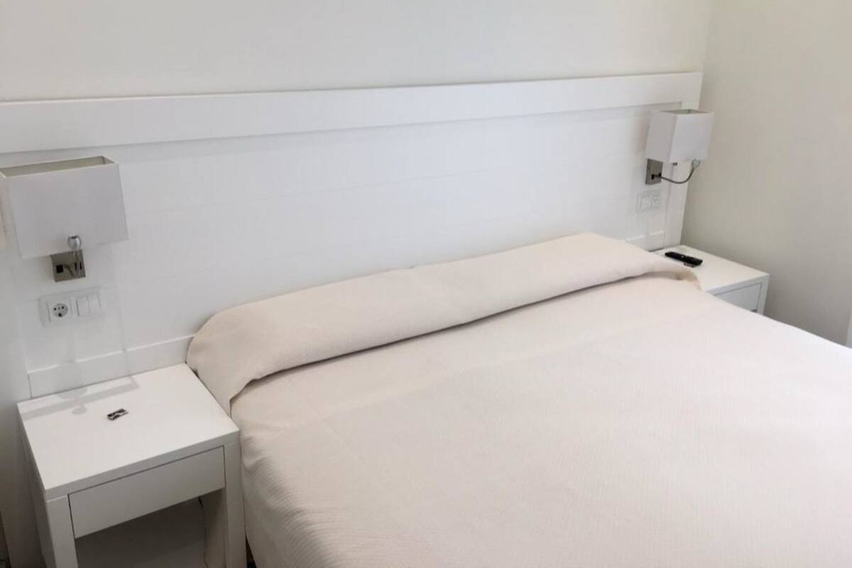 Una camera d'albergo con un letto, un comodino, una lampada e una presa di corrente.