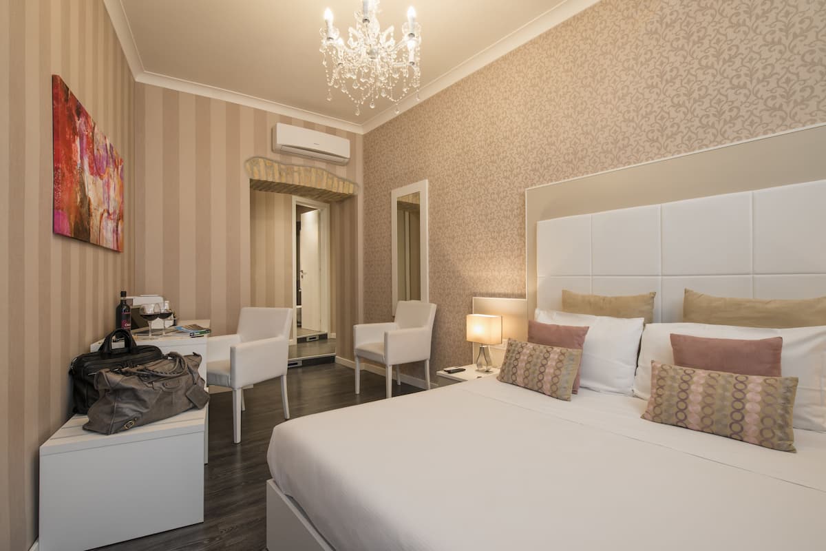 A hotel room with a large bed, a sitting area with a chair, a desk with a lamp, and a painting on the wall.