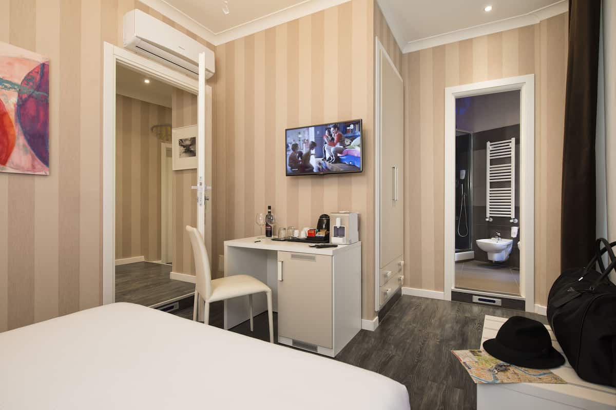 A hotel room with a bed, a desk with a chair, a TV, and a bathroom visible through an open door.