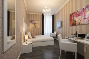 Une chambre d’hôtel moderne équipée d’un lit, d’une table de chevet, d’une lampe, d’un bureau avec un ordinateur portable, d’une chaise, d’une télévision et d’œuvres d’art accrochées au mur.