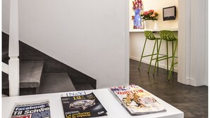 A modern interior with a staircase, a white table with magazines, and a kitchen area with stools and a vase of flowers. - Cheap & Chic Hotel (Ciutadella de Menorca)