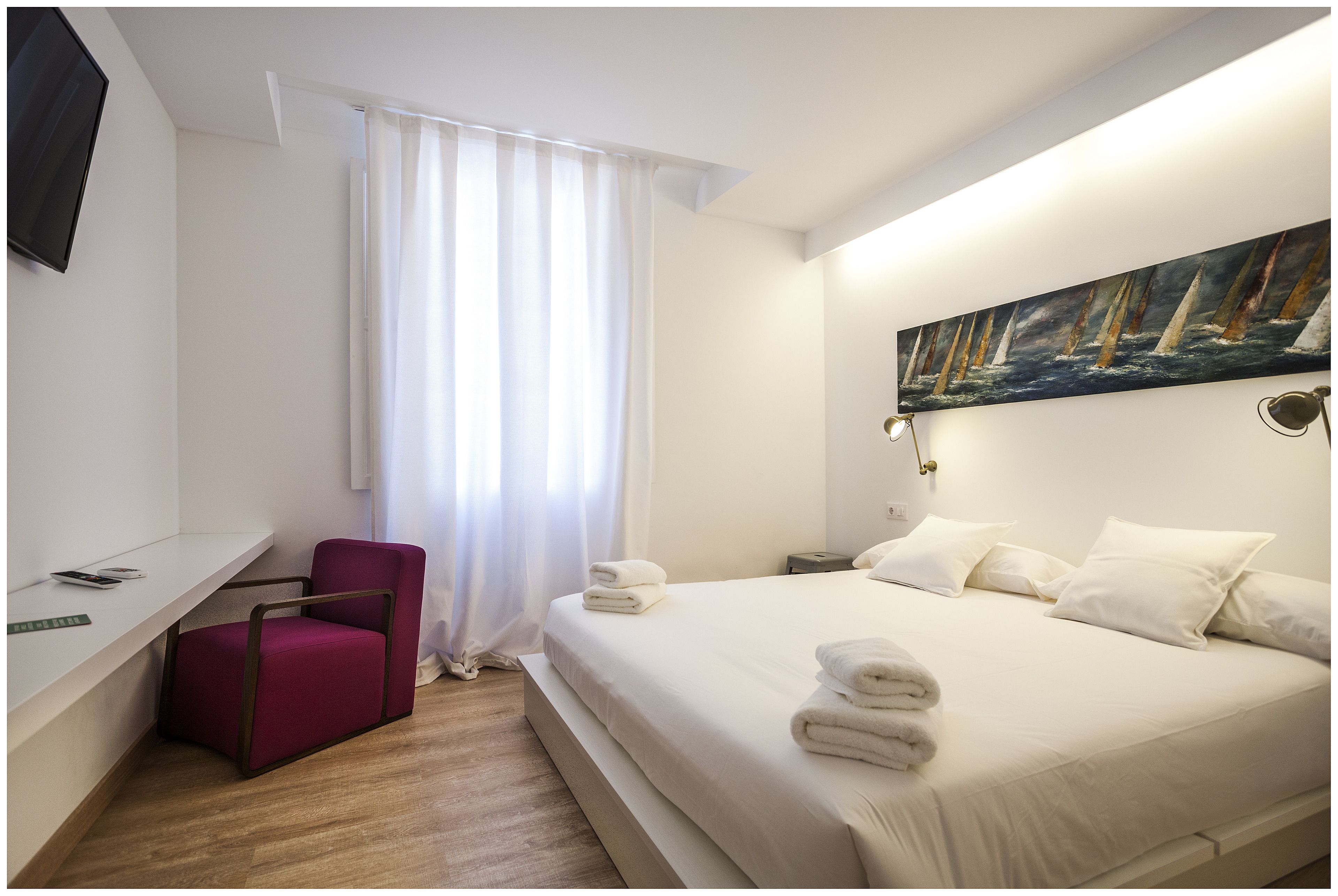 Habitación de hotel con cama, escritorio, silla, un cuadro y ventana con cortinas.