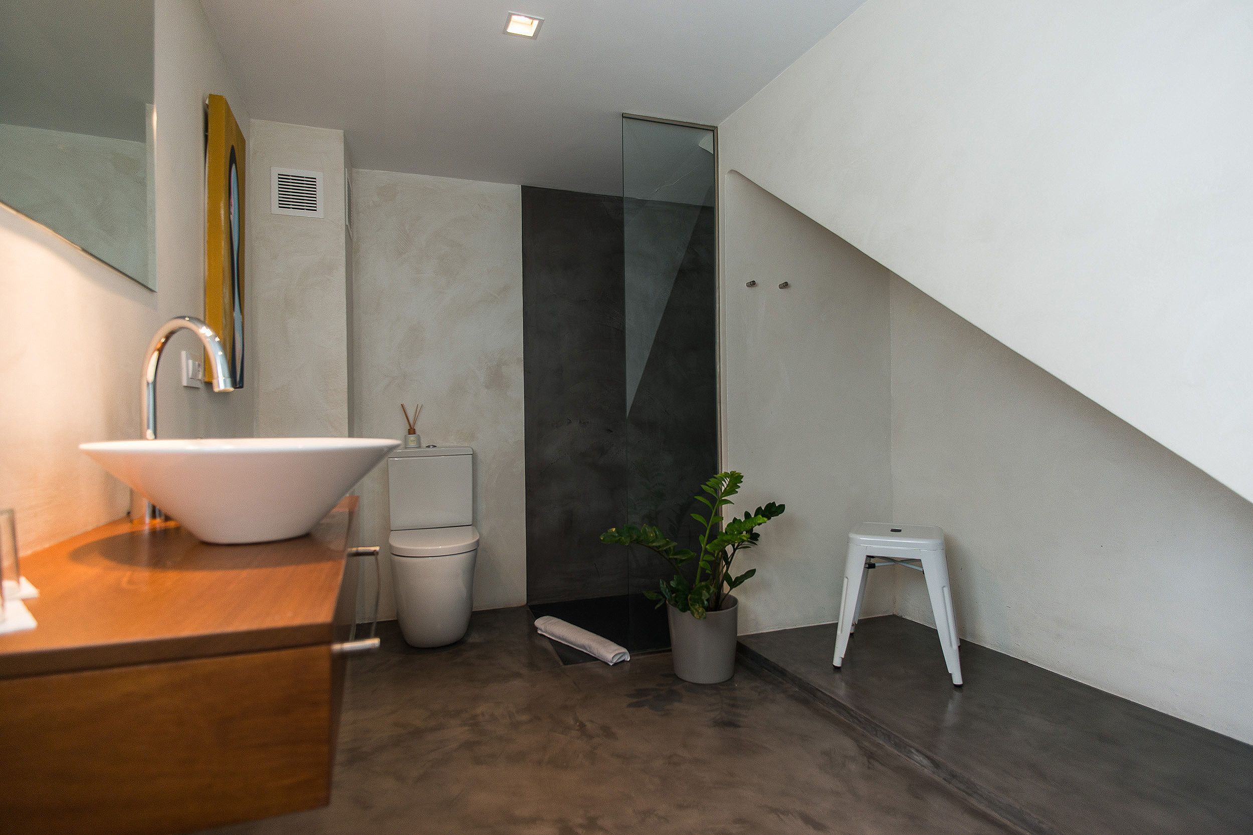 Un baño moderno con un lavamanos grande de color blanco, una cabina de ducha con paredes de vidrio y un taburete pequeño de color blanco.