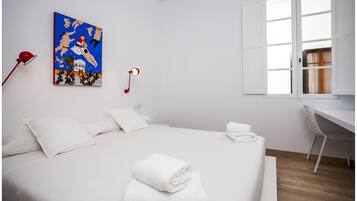 Une chambre d’hôtel au style minimaliste, dotée d’un grand lit, de linge de lit blanc, d’un bureau et d’une fenêtre avec des volets blancs.