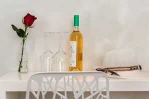Una mesa blanca con una botella de vino, dos copas de vino, una rosa y un par de tijeras.
