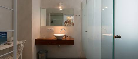Uma casa de banho moderna com cabine de duche em vidro, lavatório branco com cuba e toucador de madeira.