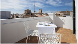 A balcony with a table set for two, white chairs, and a view of a historic building in the background. - Cheap & Chic Hotel (Ciutadella de Menorca)