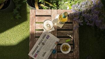 A wooden table with a newspaper, a bottle, a bowl of lemons, and a bunch of purple flowers.